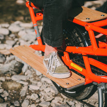 Load image into Gallery viewer, Product image showing a pair of Yuba Bamboo Sideboards for the Yuba Spicy Curry Electric Longtail Cargo Bike, with a rear passenger resting their feet on the sideboards.