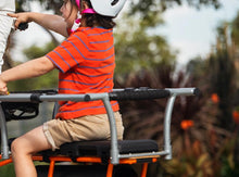 Load image into Gallery viewer, Child wearing a helmet seated on an electric cargo bike, holding padded safety bars designed for secure passenger transport.