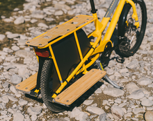 Load image into Gallery viewer, Yellow cargo bike with wooden platform on a rocky ground.