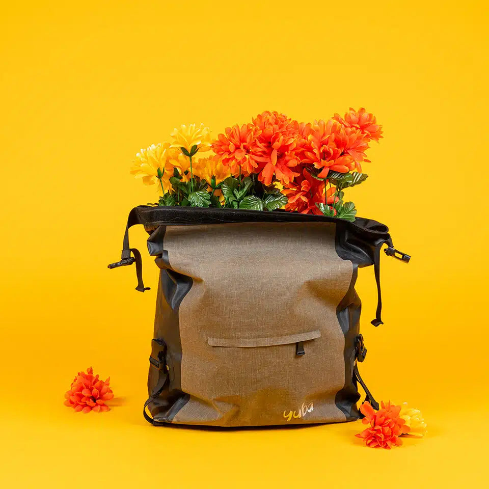 Gray and black Yuba bike bag filled with vibrant orange and yellow flowers, displayed against a bright yellow background.