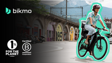 Load image into Gallery viewer, A photo of an urban setting with a woman cycling an electric bike, and the Bikmo logo overlaid on it. 
