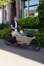 Load image into Gallery viewer, Lifestyle image of the Dolly Joy electric cargo bike showing a toddler and baby being transported in the cargo box. The parent is standing beside the cargo bike.
