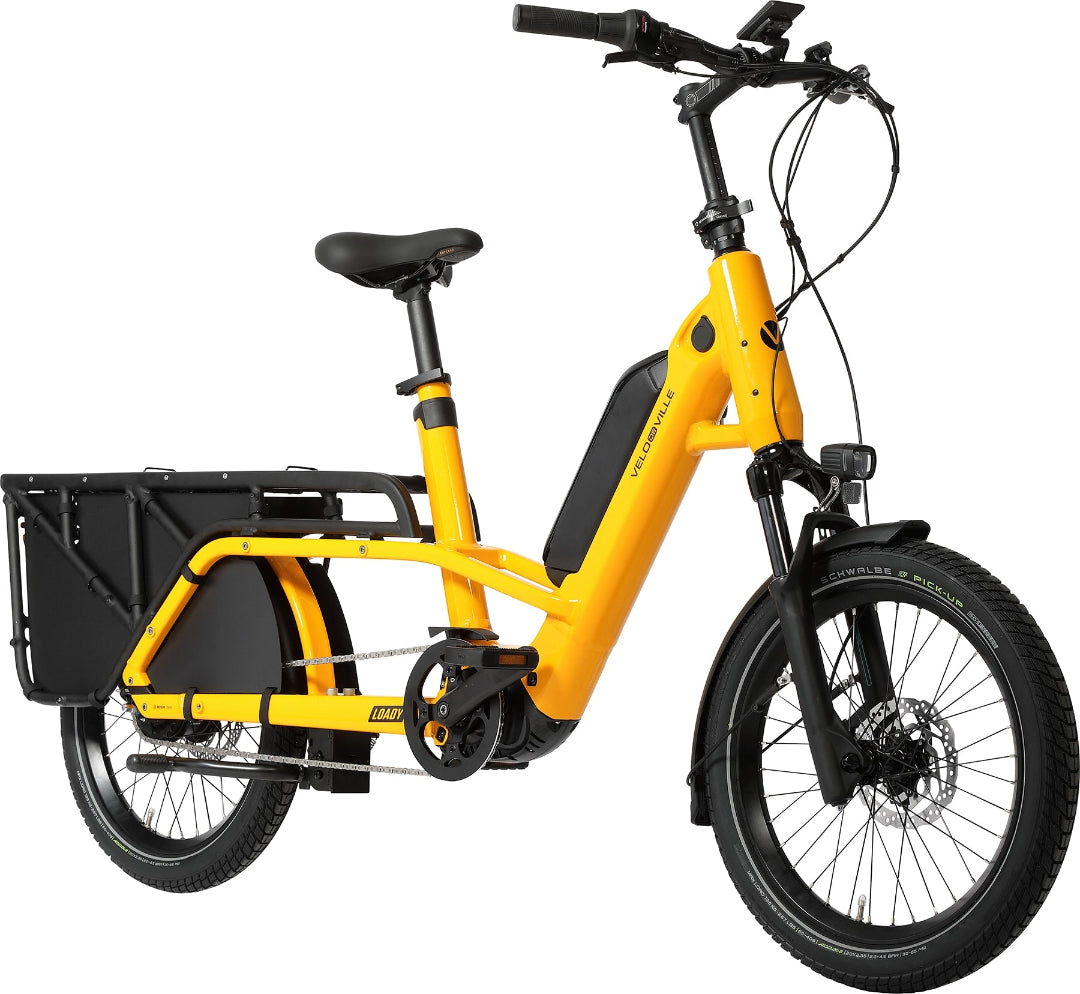 A product image of the Velo de Ville Loady electric longtail cargo bike. The frame colour is yellow. The angle of the image is from the front right of the bike.