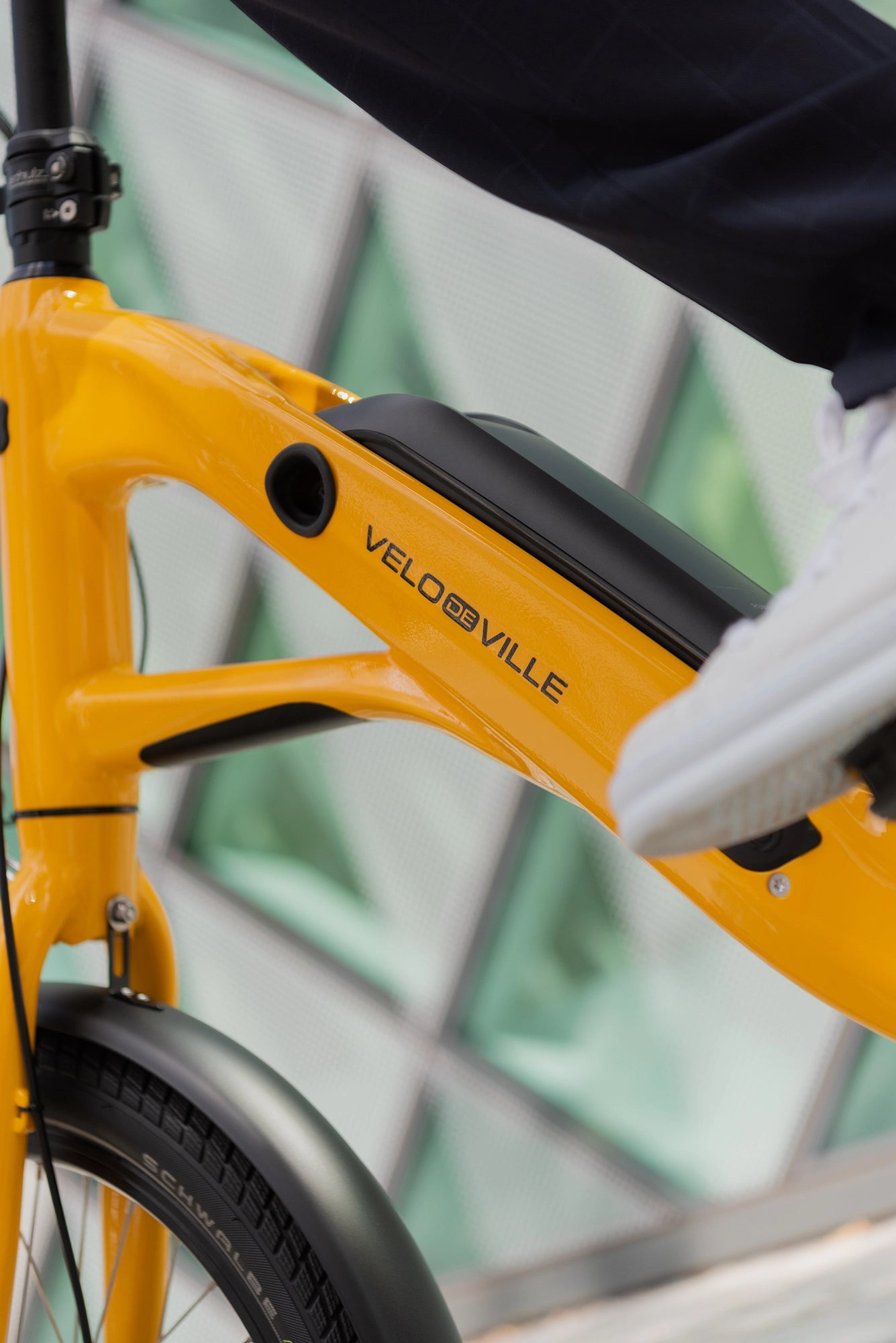 A close-up lifestyle image showing the downtube and battery of a VELO DE VILLE KEB electric bike.