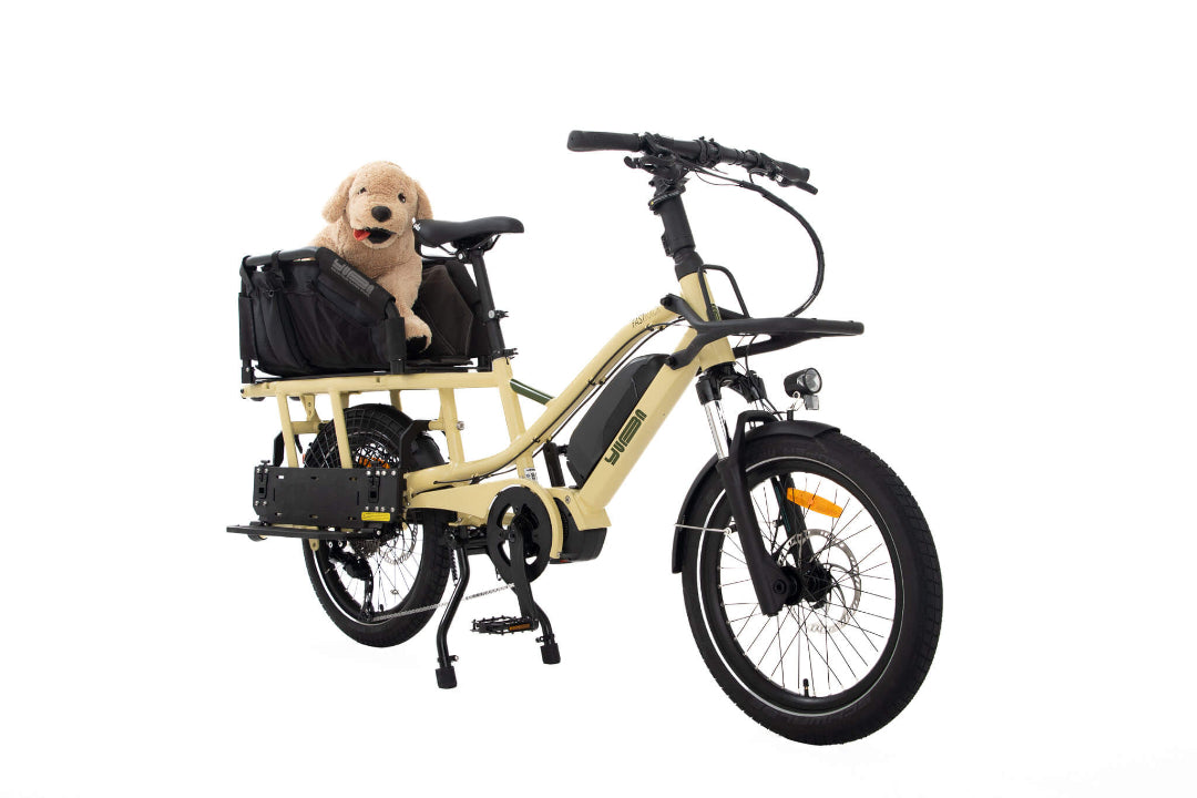 A product image of the Yuba Fastrack electric longtail cargo bike, showing the Wooftop dog carrier accessory setup with the Latte frame colour option.