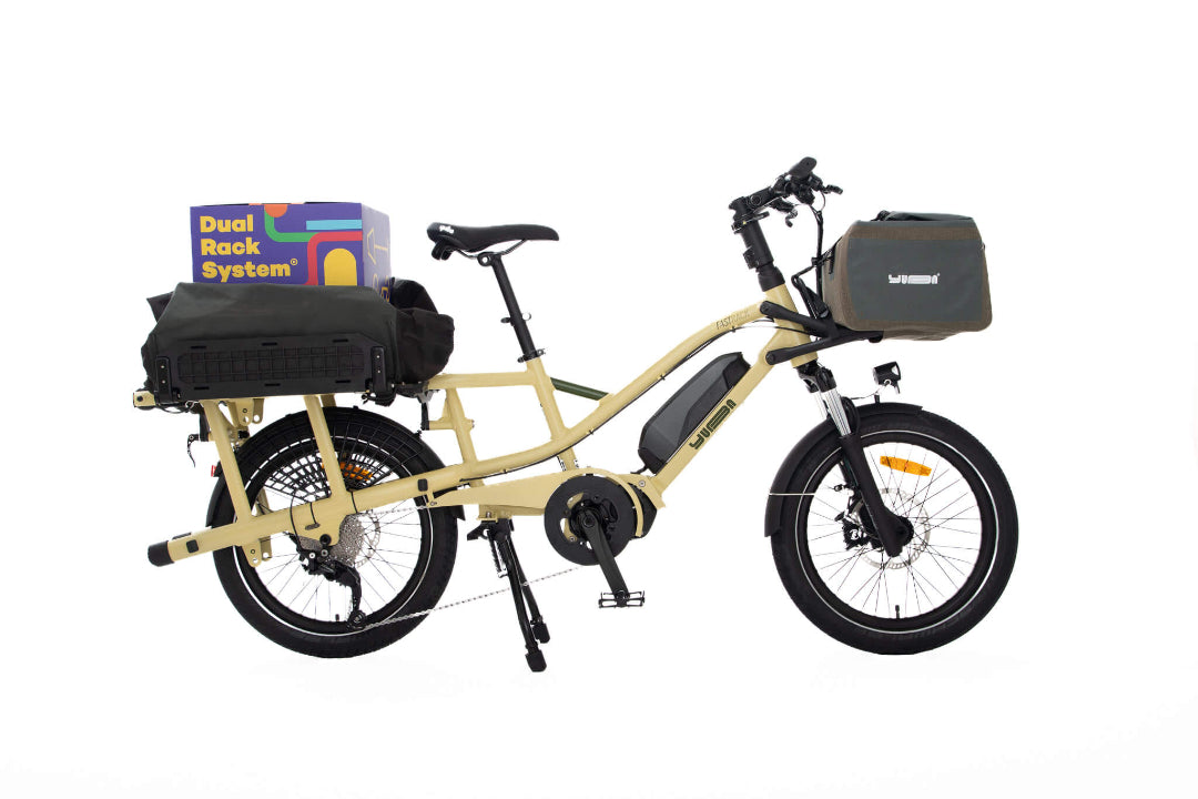 A product image of the Yuba Fastrack electric longtail cargo bike, showing the Latte frame colour option. The DRS bag and Grab and Go bag accessories are attached to the bike. 