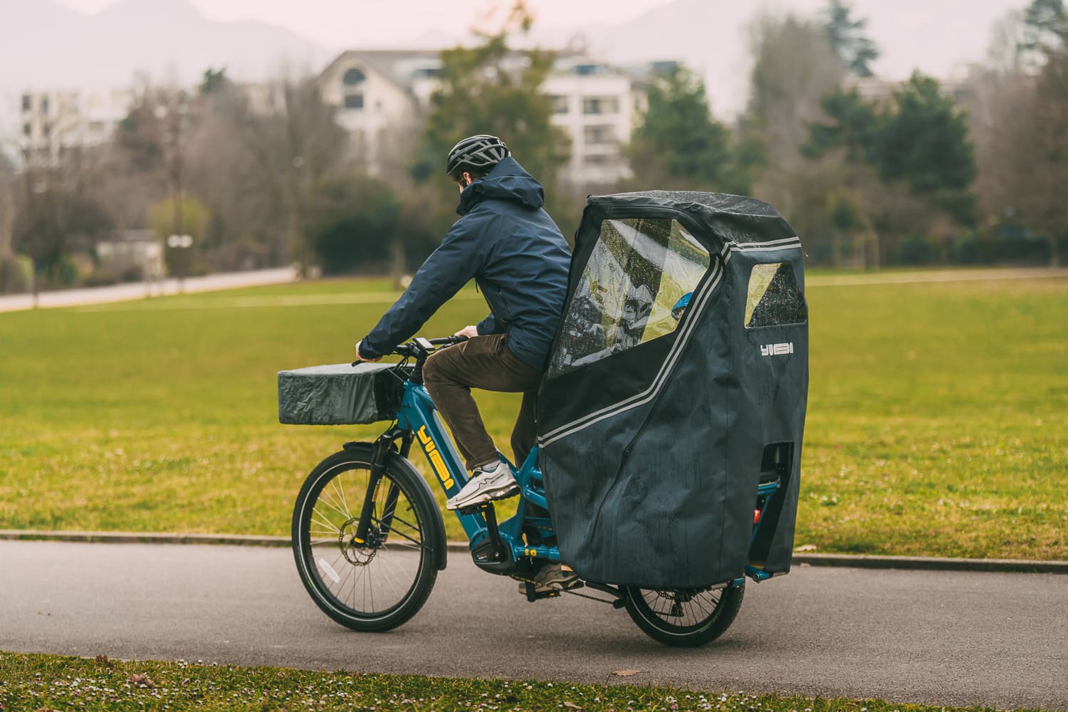 Person riding a cargo bike with a covered rear compartment on a paved path.