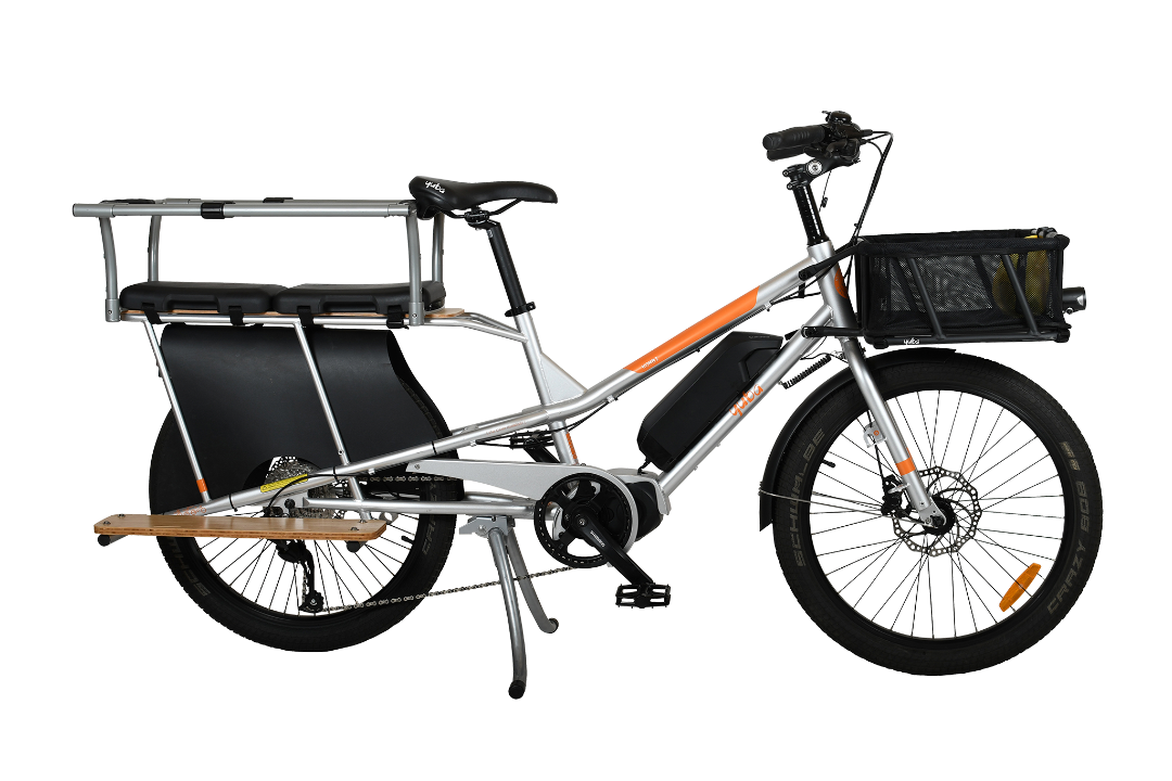 A product image of the Yuba Kombi E5 electric longtail cargo bike which can be hired from LeaseBike. The photo shows the right side of the cargo bike. The photo shows two soft spot seats and a monkey bar accessory attached to the rear rack and a bread basket attached to the front of the bike.