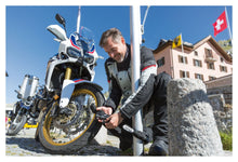 Load image into Gallery viewer, Man adjusting a motorcycle tire with a scenic background
