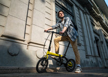Load image into Gallery viewer, Man with a yellow and black bicycle in front of a building
