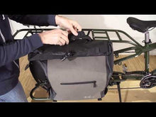 Load and play video in Gallery viewer, Hands securing a gray and black Yuba cargo bag onto the rear rack of a dark green electric cargo bike indoors.
