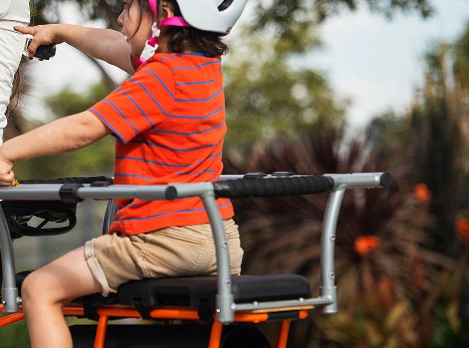 Child wearing a helmet seated on an electric cargo bike, holding padded safety bars designed for secure passenger transport.