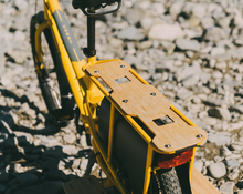 Load image into Gallery viewer, Yellow bicycle with a wooden platform on a gravel surface.
