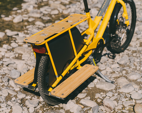 Yellow cargo bike with wooden platform on a rocky ground.
